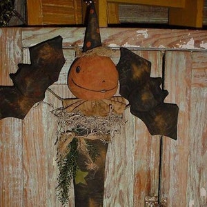 Puede incluir: Una media de Halloween hecha a mano con una cara de calabaza, alas de murciélago y un sombrero de bruja. La media está decorada con estrellas y una rama de vegetación.