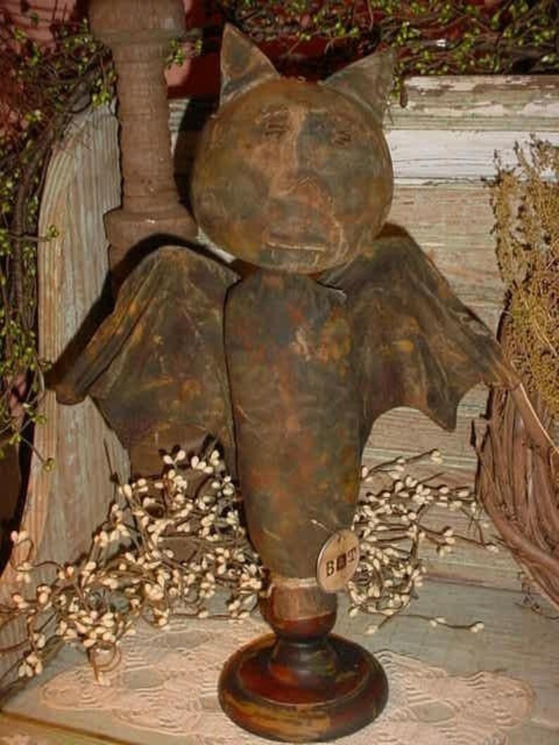 May include: A rustic, handmade, brown and green bat figurine with a painted face and wings. The bat is standing on a wooden base with a small tag that reads "GHOST".