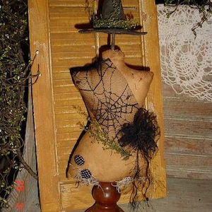 Könnte beinhalten: Eine Vintage-Hexe-Puppe mit einem schwarzen Hut und einem Spinnennetz-Design auf ihrem Kleid. Die Puppe ist aus Stoff und hat einen Holzsockel.