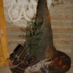 May include: A brown witch's hat with a black and brown striped ribbon and a frayed trim. The hat is decorated with dried greenery and has a small metal bell on the top.