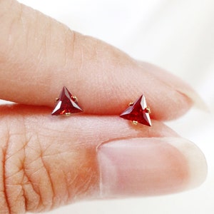 May include: A pair of gold triangle stud earrings with red gemstones.