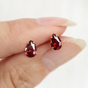 May include: A pair of gold stud earrings with pear-shaped red gemstones.