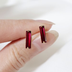 May include: A pair of gold stud earrings with red rectangular gemstones.