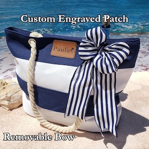 May include: A navy blue and white striped tote bag with a rope handle and a large striped bow. The bag has a custom engraved patch that reads "Paula". The text "Custom Engraved Patch" and "Removable Bow" are also visible.