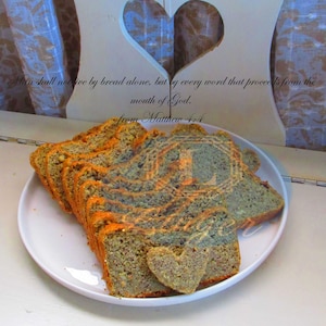 Op de afbeelding: Gesneden brood met oranje en grijze marmering, gerangschikt op een wit bord. Een hartvormig stuk brood ligt vooraan. De tekst "Man shall not live by bread alone..." is zichtbaar.