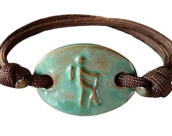 May include: A brown cord bracelet with a teal oval charm featuring a stylized hiker figure.