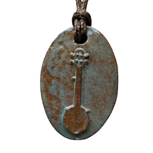 May include: A ceramic pendant with a banjo design. The oval-shaped pendant has a turquoise and brown mottled finish. A dark brown cord is attached at the top. The banjo is a darker brown color and is centered on the pendant.