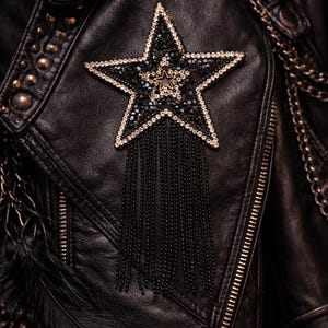 Peut inclure: Veste en cuir noir ornée d'un motif en forme d'étoile. L'étoile est décorée de perles noires et argentées, avec une étoile dorée au centre. Des franges de perles noires pendent de l'étoile. La veste a des clous dorés et une fermeture éclair.