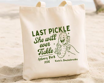May include: A cream-coloured canvas tote bag with two handles, featuring a dark green graphic of a laughing pickle being tickled by a hand wearing a ring. The text reads: LAST PICKLE She will ever Tickle Asbury Park 2026 Kate's Bachelorette.
