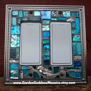 May include: A light switch cover with a mosaic design featuring blue and green glass tiles. The mosaic design includes a mermaid and the text "www.GardenGoddessMosaics.etsy.com".