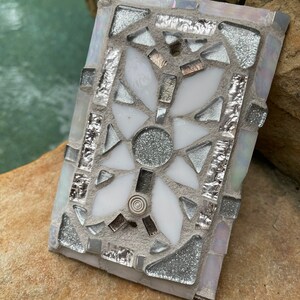 Puede incluir: Un azulejo de mosaico blanco y plateado con un dise&ntilde;o geom&eacute;trico. El azulejo est&aacute; hecho de peque&ntilde;os trozos de vidrio y tiene un acabado brillante.