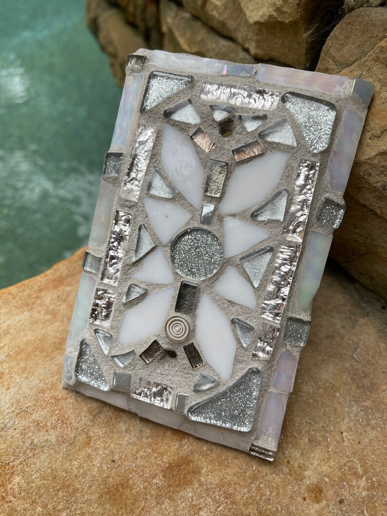 Puede incluir: Un azulejo de mosaico blanco y plateado con un dise&ntilde;o geom&eacute;trico. El azulejo est&aacute; hecho de peque&ntilde;os trozos de vidrio y tiene un acabado brillante.