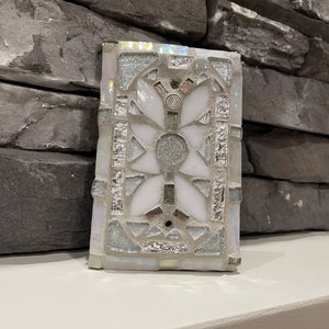 Puede incluir: Un azulejo de mosaico blanco y plateado con un dise&ntilde;o geom&eacute;trico. El azulejo est&aacute; hecho de peque&ntilde;os trozos de vidrio y tiene un acabado brillante.