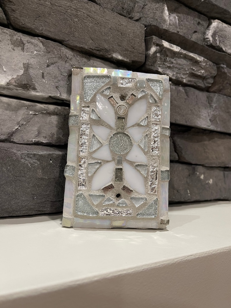 Puede incluir: Un azulejo de mosaico blanco y plateado con un dise&ntilde;o geom&eacute;trico. El azulejo est&aacute; hecho de peque&ntilde;os trozos de vidrio y tiene un acabado brillante.