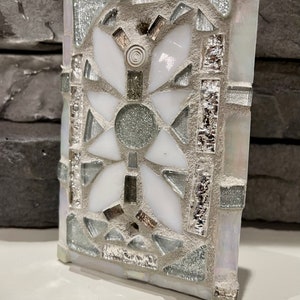 Puede incluir: Un azulejo de mosaico blanco y plateado con un dise&ntilde;o geom&eacute;trico. El azulejo est&aacute; hecho de peque&ntilde;os trozos de vidrio y est&aacute; colocado en un mortero blanco.