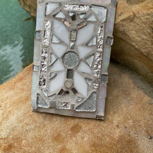 Puede incluir: Un azulejo de mosaico blanco y plateado con un dise&ntilde;o geom&eacute;trico. El azulejo est&aacute; hecho de peque&ntilde;os trozos de vidrio y tiene un acabado brillante.