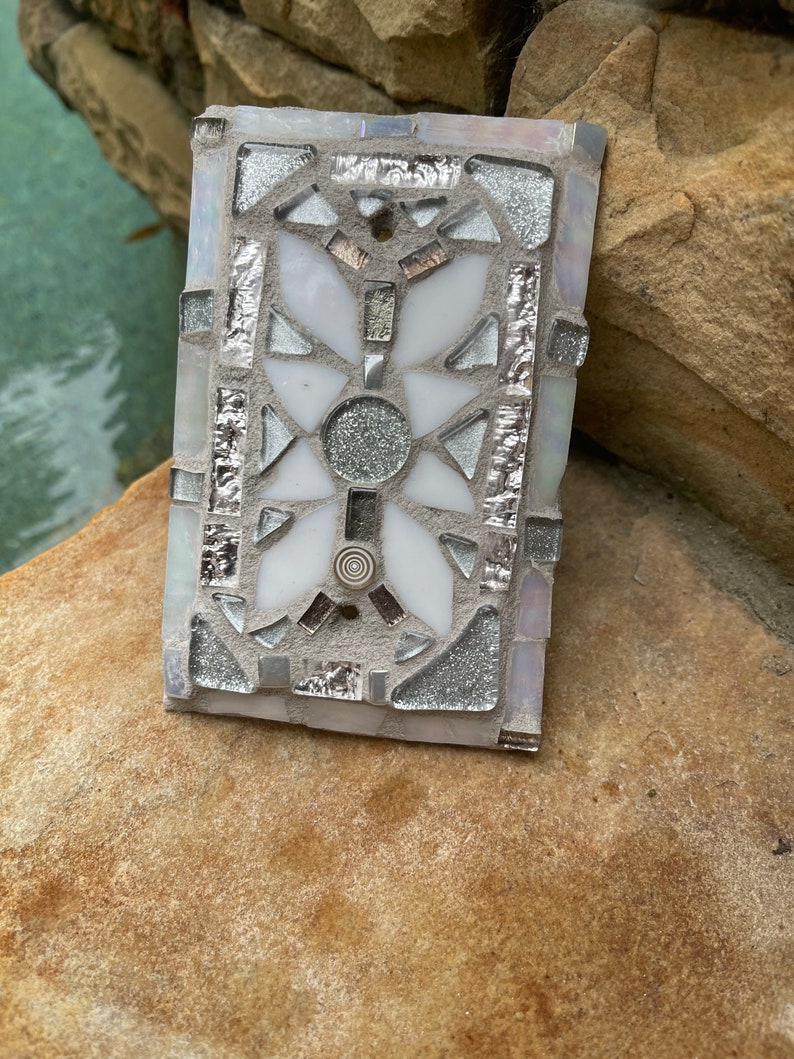 Puede incluir: Un azulejo de mosaico blanco y plateado con un dise&ntilde;o geom&eacute;trico. El azulejo est&aacute; hecho de peque&ntilde;os trozos de vidrio y tiene un acabado brillante.