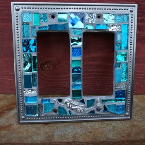 May include: A silver double light switch cover with a mosaic design featuring blue and turquoise glass tiles. A mermaid is featured in the centre of the design.