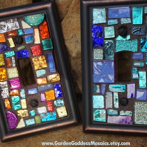 May include: Two decorative light switch covers with mosaic tile designs. One cover features a colorful mosaic with gold, silver, and blue tiles. The other cover features a blue and turquoise mosaic with iridescent tiles.