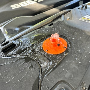 May include: A close-up of a water jet spraying from a round orange nozzle on a black surface. The water is flowing down the surface, creating a wet, shiny effect.