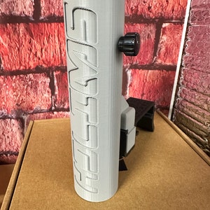 Puede incluir: Un soporte para tel&eacute;fono impreso en 3D de color gris con la palabra "SMYTH" impresa en el lateral. El soporte tiene una perilla negra para ajustar el &aacute;ngulo.