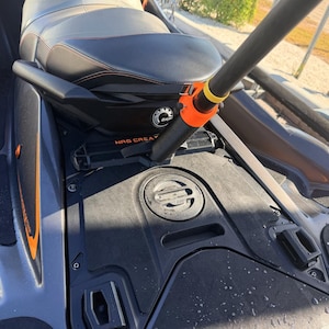 Könnte beinhalten: Ein dunkelgrauer Jetski mit schwarzem Sitz und orangefarbenen Nähten, einer runden Stauklappe und einem schwarzen Rutenhalter hinter dem Sitz, der mit einer leuchtend orangefarbenen Klemme und einem gelben Ring versehen ist, beschriftet mit NRG CREATIVE.