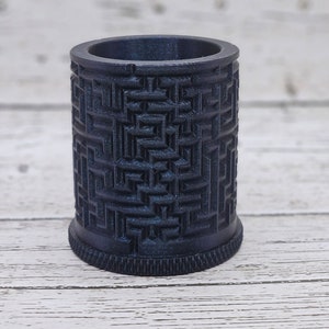 May include: A dark blue cylindrical container with a geometric pattern. The container has a textured surface and a slightly rounded bottom.