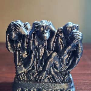 May include: A three-dimensional sculpture of three monkeys, each covering a different part of their face. The monkey on the left is covering its eyes, the middle monkey is covering its ears, and the monkey on the right is covering its mouth. The sculpture is made of a dark gray material and has a textured surface.