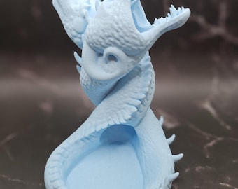 May include: A light blue 3D printed dragon head dice holder with an open mouth and a small, round, open space inside for dice.