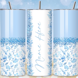 May include: A light blue tumbler with a floral design and the text "Name Here". The tumbler features a blue glitter band and a floral pattern at the bottom. It includes a silver straw.