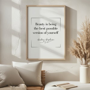 Puede incluir: Una impresión enmarcada con fondo blanco y texto negro que dice "Beauty is being the best possible version of yourself" con la firma "Audrey Hepburn" debajo. La impresión está en un marco de madera y está colgada en una pared blanca.