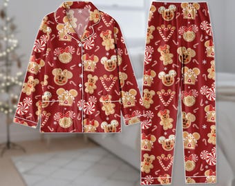 May include: Red pajama set featuring a repeating pattern of gingerbread Mickey Mouse heads, gingerbread houses, and candy canes. The long-sleeved top has white trim and buttons. The matching pants complete the festive sleepwear ensemble.