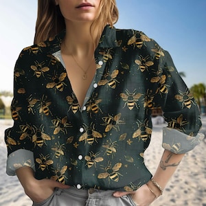May include: Dark green button-down shirt with a repeating pattern of gold and black bees. The long-sleeved shirt has a classic collar and white buttons. The cuffs are rolled up, revealing a patterned interior.