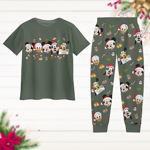 May include: Green pyjama set featuring Mickey Mouse, Donald Duck, and Goofy in Santa hats. The short-sleeved top has a graphic of the characters with Christmas lights. The trousers have a repeating pattern of the characters, candy canes, and bells.