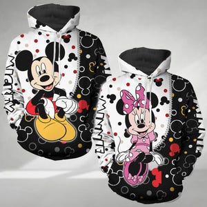 Puede incluir: Sudadera con capucha negra y blanca con un diseño de Mickey Mouse rojo, amarillo y negro en la parte delantera. La sudadera también tiene un patrón de lunares negros y blancos y el texto "Mickey" y "Minnie" en los lados.