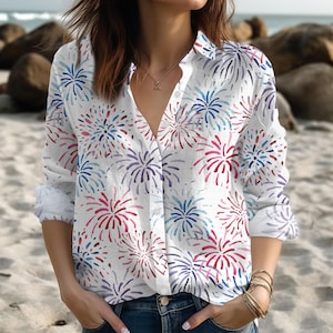 May include: White button-down shirt with a colorful firework pattern in red, blue, and purple. The long-sleeved shirt has a V-neck and is paired with blue jeans. The shirt is made of a lightweight fabric, perfect for warm weather.