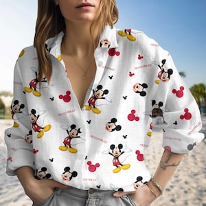 May include: White button-down shirt with a repeating pattern of Mickey Mouse illustrations and red Mickey Mouse head shapes. The words "MICKEY MOUSE" are printed on the shirt. The shirt has long sleeves and a collared neckline.