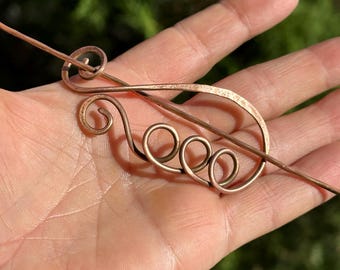 May include: A copper hair stick with a decorative swirl design. The stick is about 6 inches long and has a smooth, polished finish.