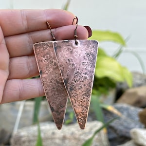May include: A pair of copper triangle earrings with a hammered texture. The earrings are a light copper color and have a simple design.