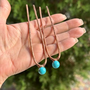 May include: Two copper hair pins with turquoise beads at the end. The pins are hammered and have a rustic look.