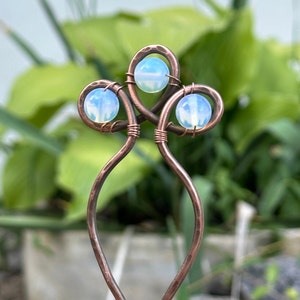 May include: A copper wire hair stick with three opal stones. The wire is twisted and hammered to create a unique design. The opal stones are a light blue color.