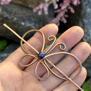May include: A copper butterfly hair stick with a dark pearl accent. The stick is hammered for texture and has a simple, elegant design.