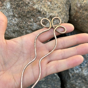 May include: A copper hair stick with a decorative knot at the top. The stick is hammered and has a textured surface.