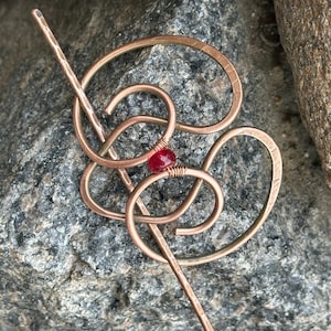 May include: A copper hair stick with a red glass bead in the center. The stick is twisted into a decorative shape.