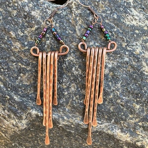 May include: Copper earrings with a hammered finish and iridescent beads. The earrings are long and dangle, with a triangular shape at the top.