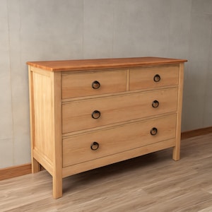 Op de afbeelding: Een lichtgekleurde houten dressoir met vier lades en een bovenste gedeelte met twee kleinere lades. De dressoir heeft zwarte ronde handgrepen en een roodbruin bovenblad. De dressoir is gemaakt van lichtgekleurd hout.