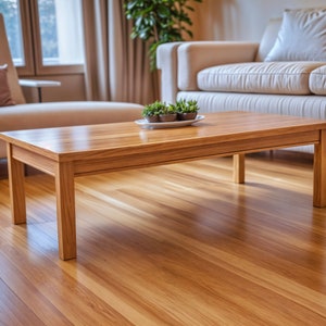 Könnte beinhalten: Ein heller Holz-Couchtisch mit einer rechteckigen Tischplatte und einer Schublade. Der Tisch hat vier Beine und steht auf einem Hartholzboden. Auf dem Tisch stehen kleine Topfpflanzen.