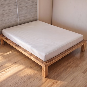 May include: A wooden bed frame with a white mattress. The bed frame is made of natural wood with a light brown finish. The bed frame has a simple design with a rectangular shape and four legs.