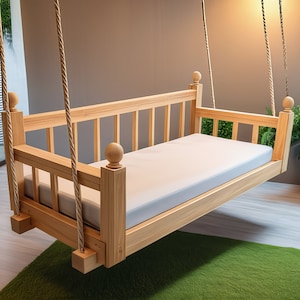 Könnte beinhalten: Ein Holz-Schaukelbett mit einer weißen Matratze, das mit dicken Seilen von der Decke hängt. Das Schaukelbett ist aus Naturholz gefertigt und hat ein schlichtes Design.