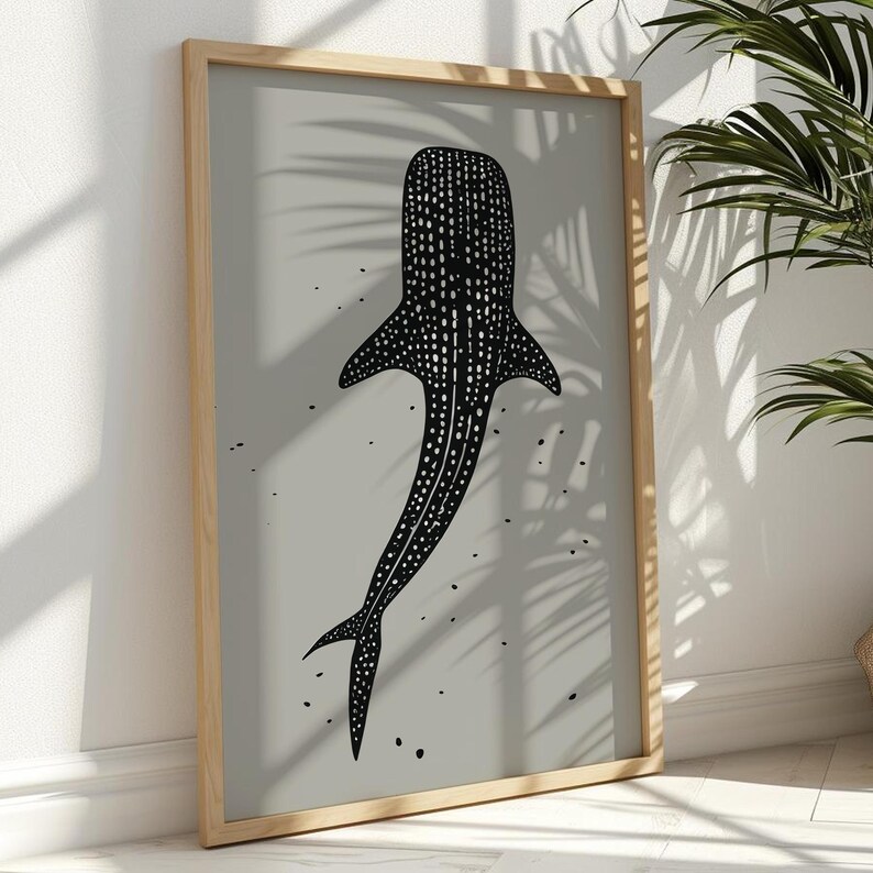Minimalist illustration print depicting a whale shark swimming in the ocean in an elegant manner, the shark is drawn in a black color with white dots and the background is a beige color with black ink spots, it is hanging in a elegant living room